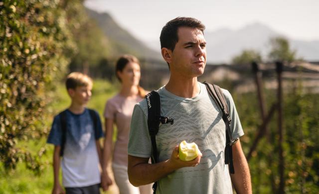 Familie beim Wandern durch Apfelwiesen in Südtirol.