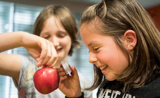 Zwei Kinder betrachten mit einer Lupe einen Südtiroler Apfel und haben dabei viel Spaß.